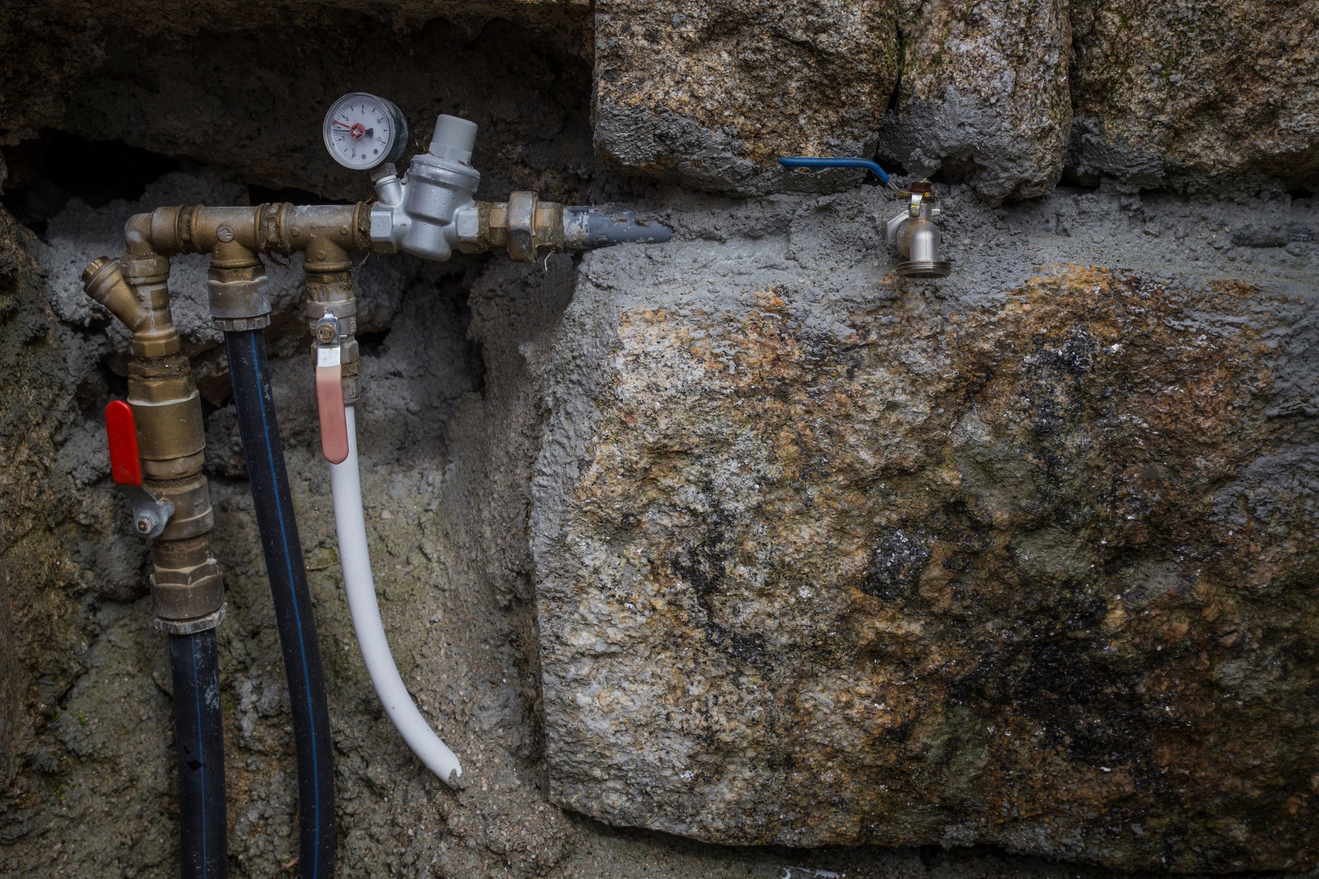 Detalhe de uma torneira com uma válvula de controle de pressão em uma parede de pedra escura e antiquada.